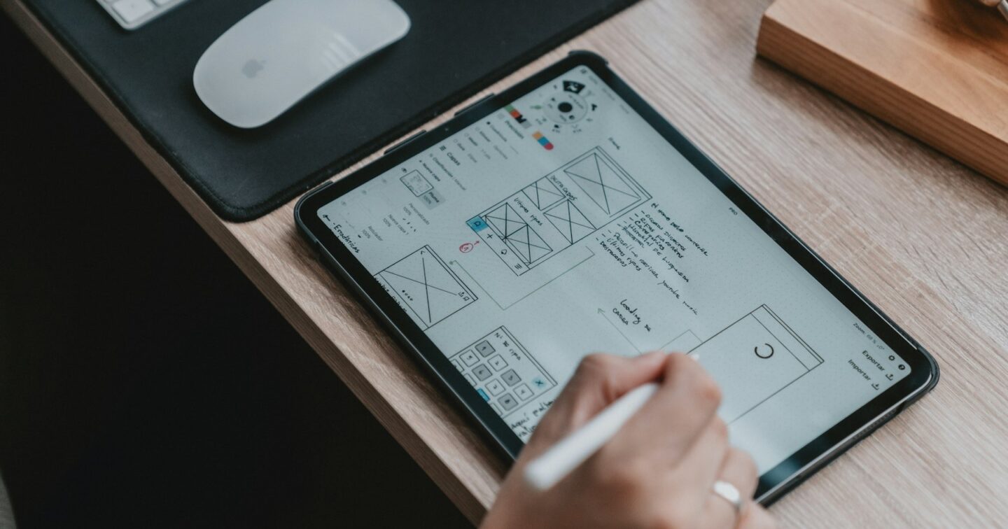 Hand sketching a website wireframe with a stylus on a tablet next to a keyboard and mouse