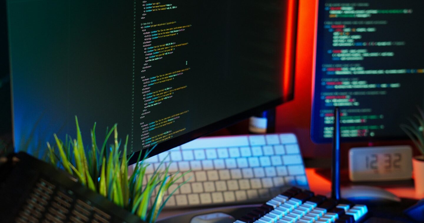 Two monitors showing source code beside keyboards on a developer desk