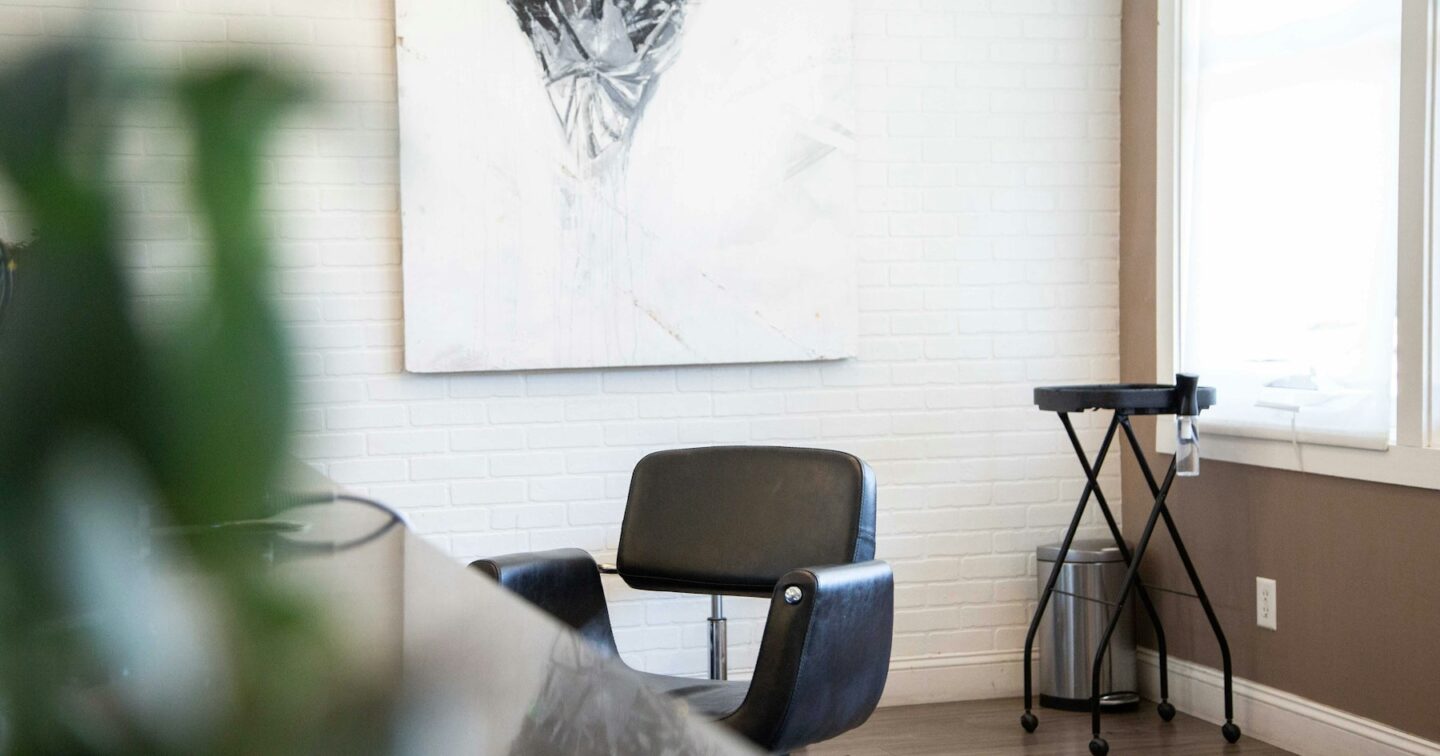 An empty black styling chair in a bright, quiet hair salon