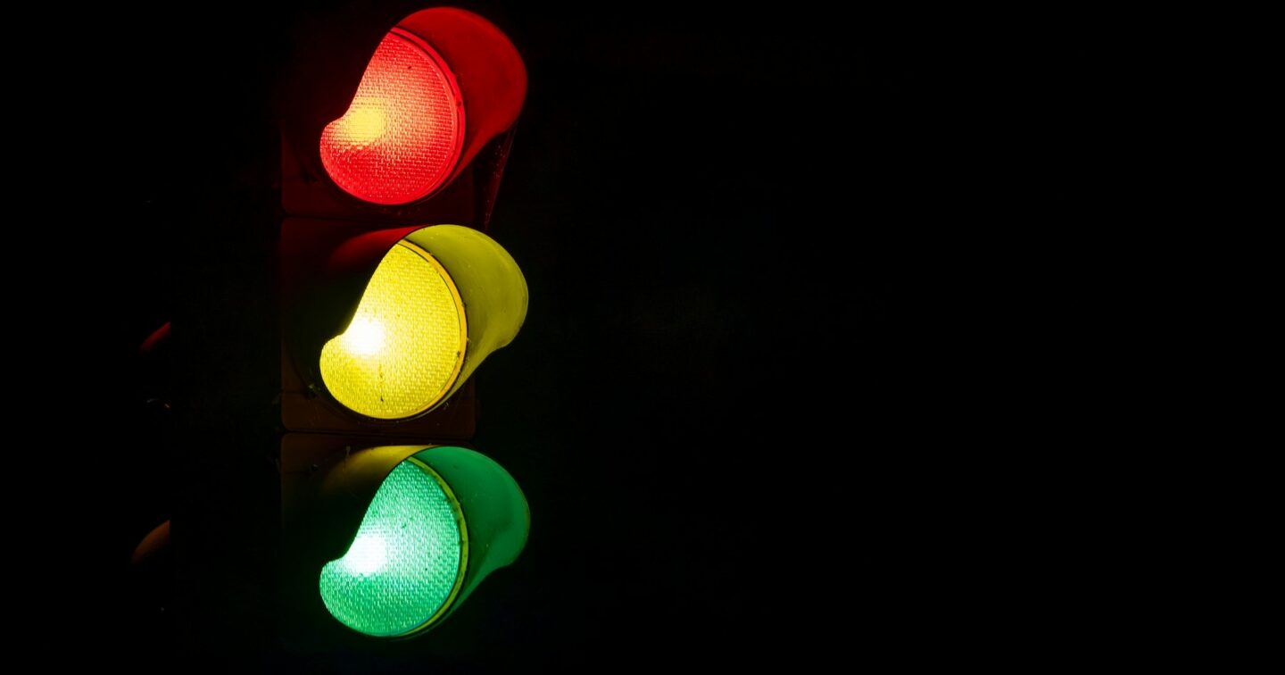 A traffic light glowing red, amber and green against a dark background