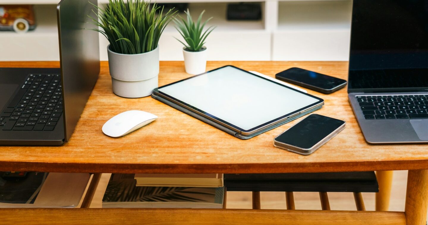 Laptops, a tablet and two smartphones on a wooden desk, representing one content source feeding several devices