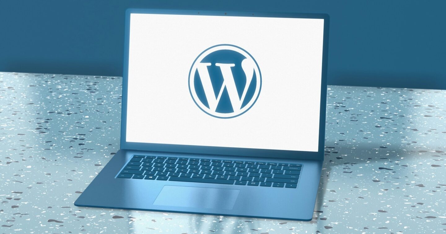 Laptop on a speckled blue surface showing the WordPress logo on its screen