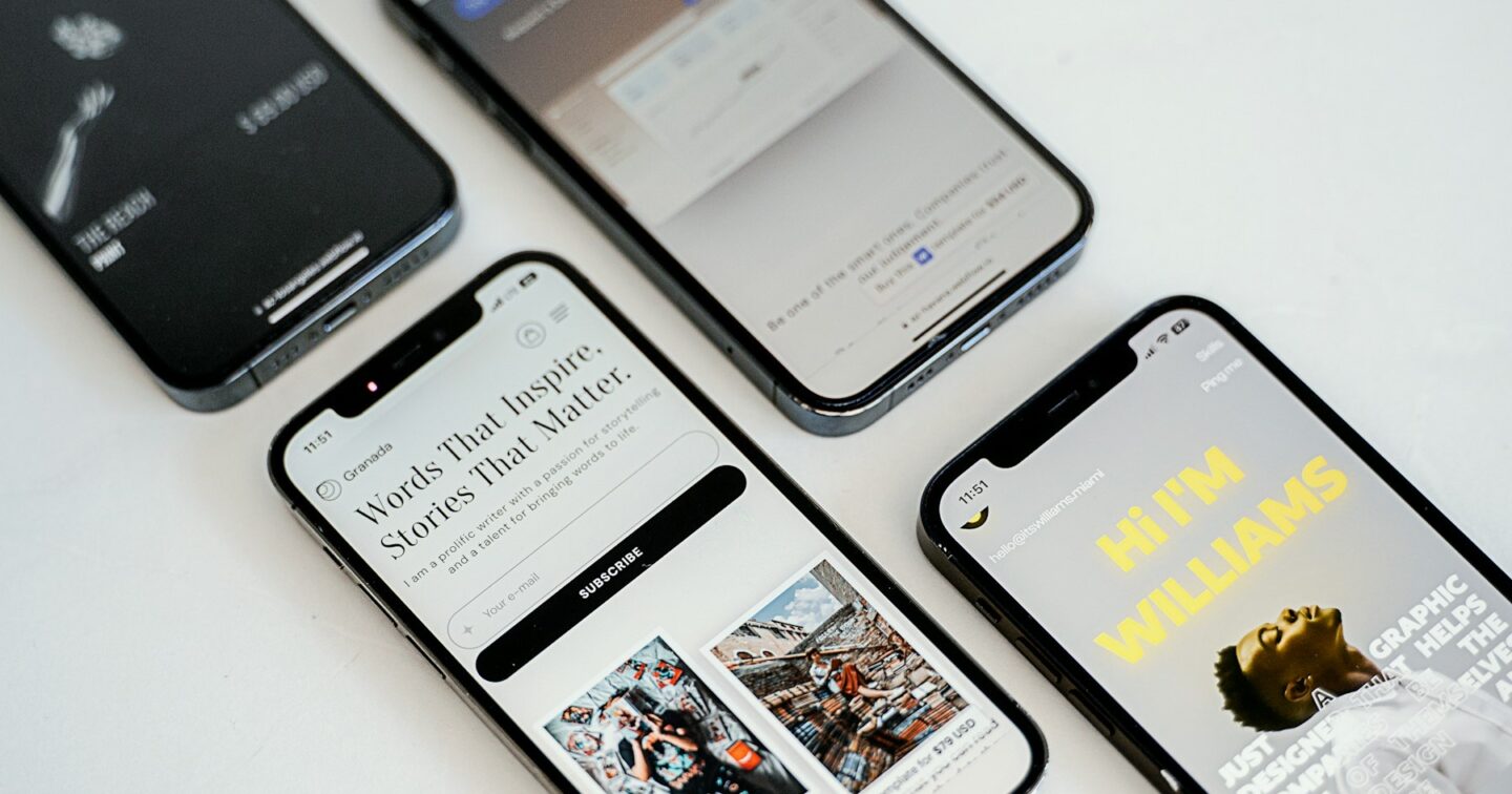 Four smartphones on a white desk, each showing a different mobile website layout
