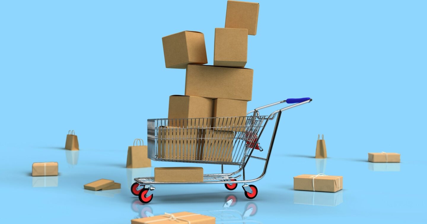 Shopping trolley piled high with brown cardboard boxes, surrounded by parcels and paper bags on a light blue background