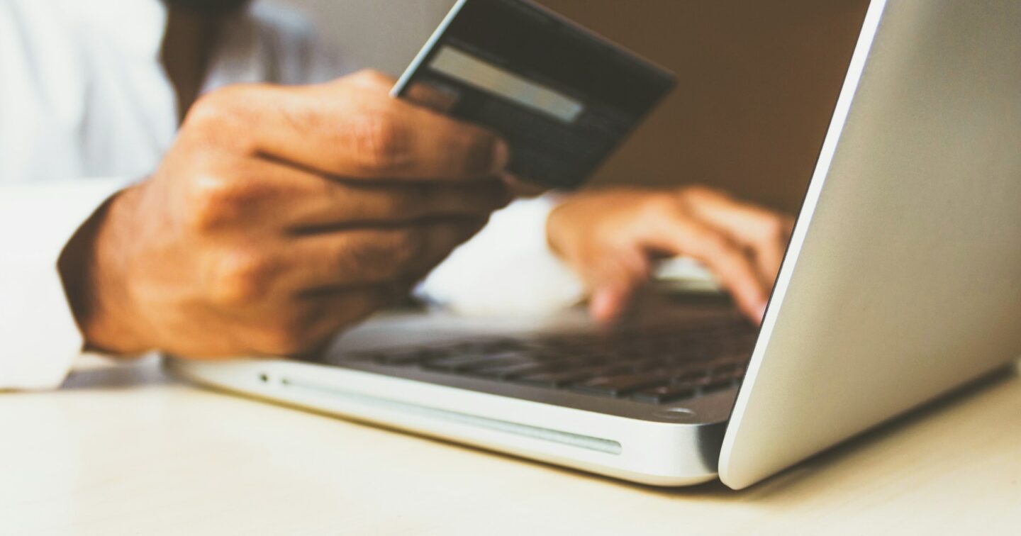 Person holding a bank card while typing on a laptop to pay for an online order