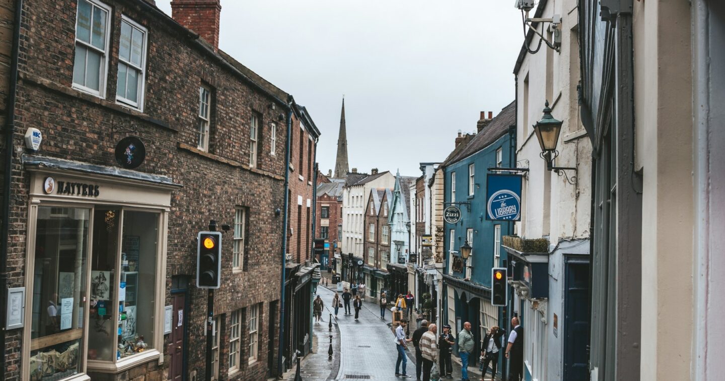 Narrow English market-town street with independent shops and a church spire in the distance