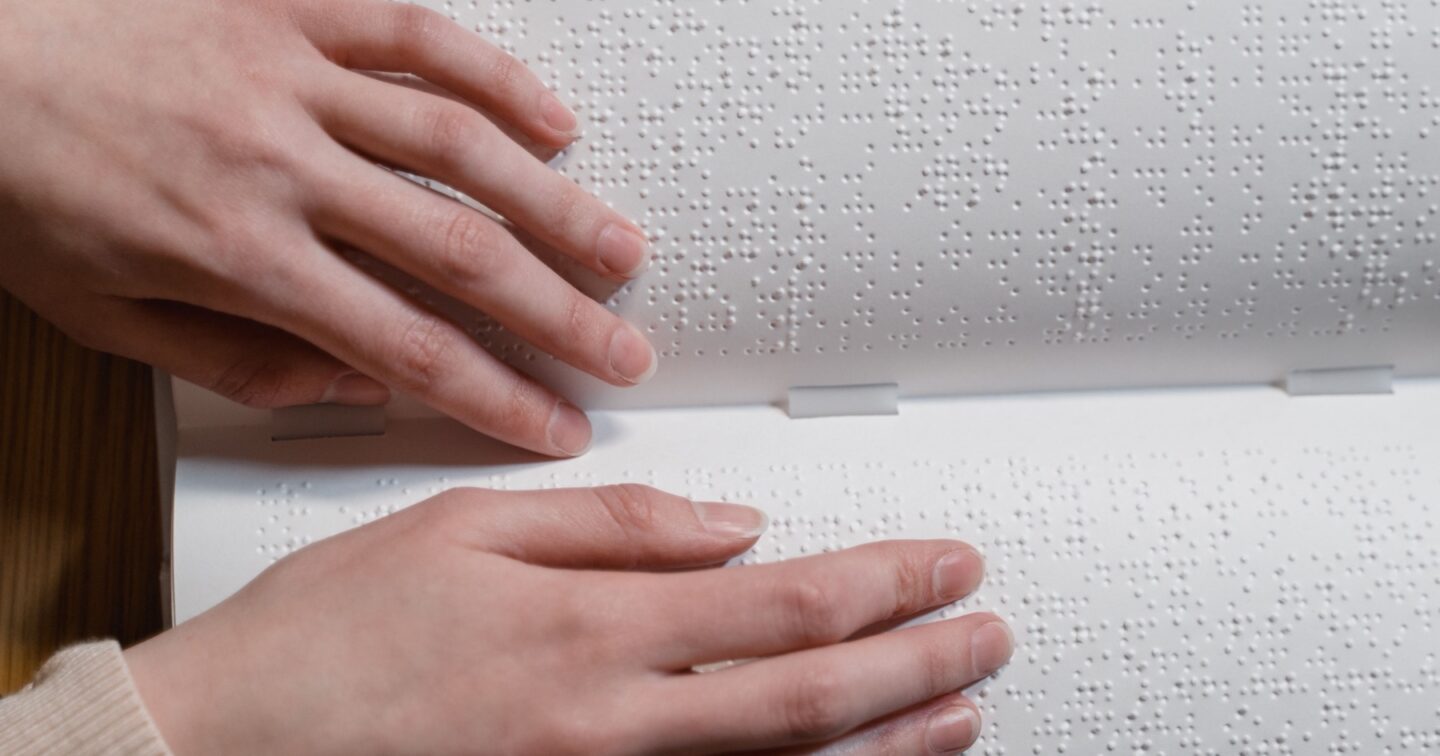 Close-up of two hands reading the raised dots of an open braille book
