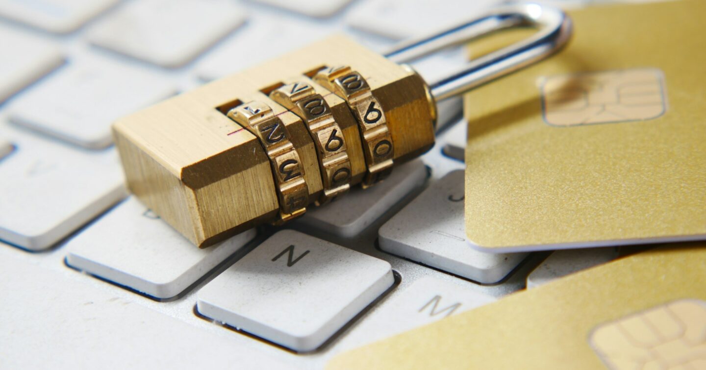Brass combination padlock resting on a white computer keyboard next to bank cards, representing website and payment security