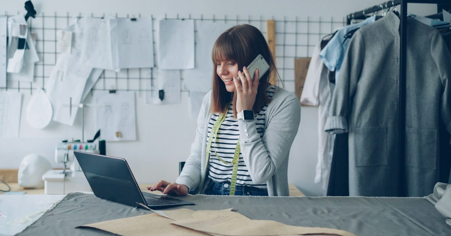 Small business owner on the phone while working on a laptop in her clothing studio