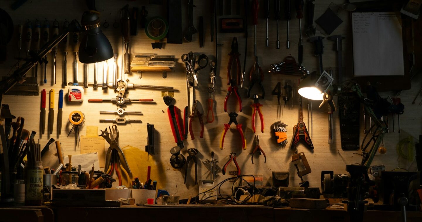 A workshop wall of hand tools hanging above a workbench, lit by two small desk lamps