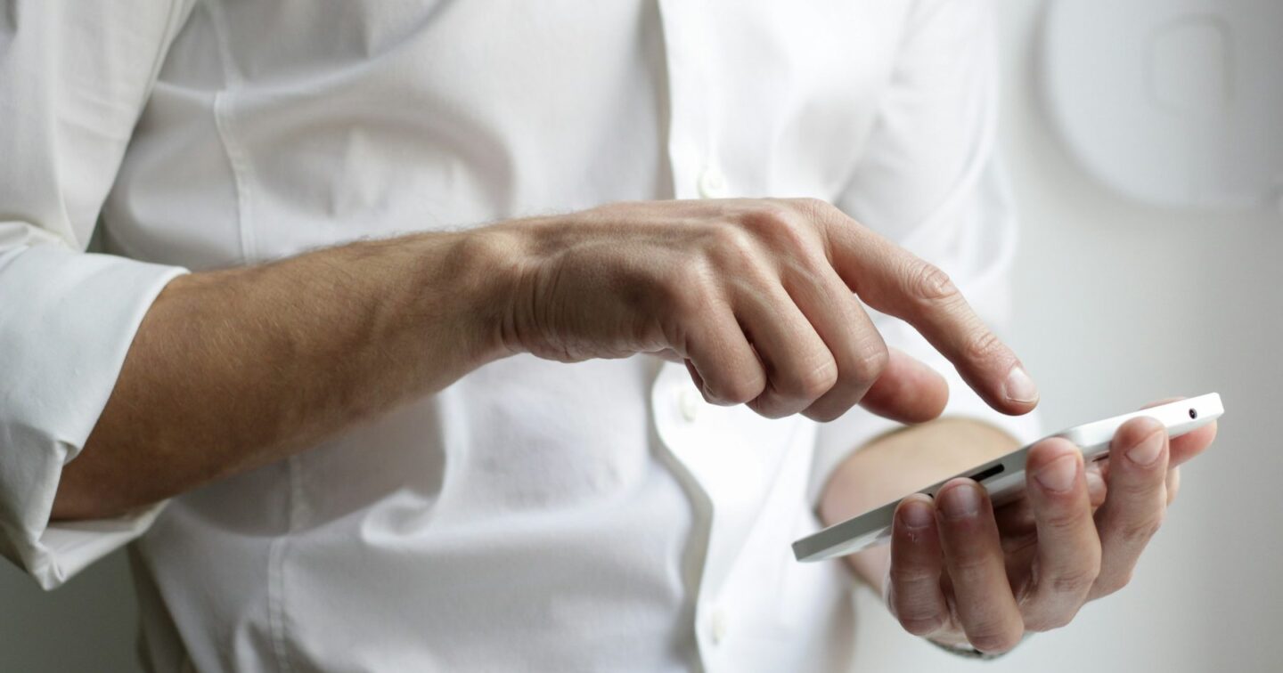 Close-up of a person in a white shirt tapping a message on a smartphone, representing a customer asking a question through an AI chatbot on a business website