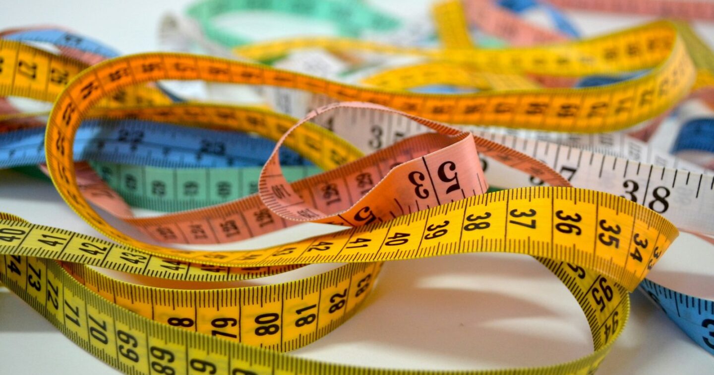 Tangled yellow, orange, pink and blue tailor's tape measures on a white table, representing software that is measured and priced to fit one business