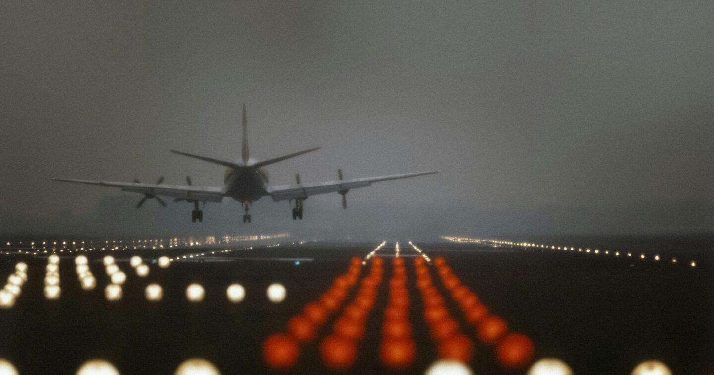 An aircraft seen from behind as it comes in to land along rows of glowing runway lights at dusk, a visual metaphor for guiding visitors to a landing page