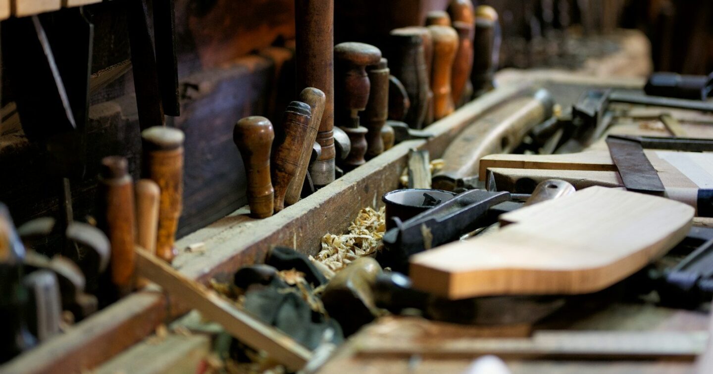 Old wooden-handled chisels and hand planes on a carpenter’s workbench covered in wood shavings