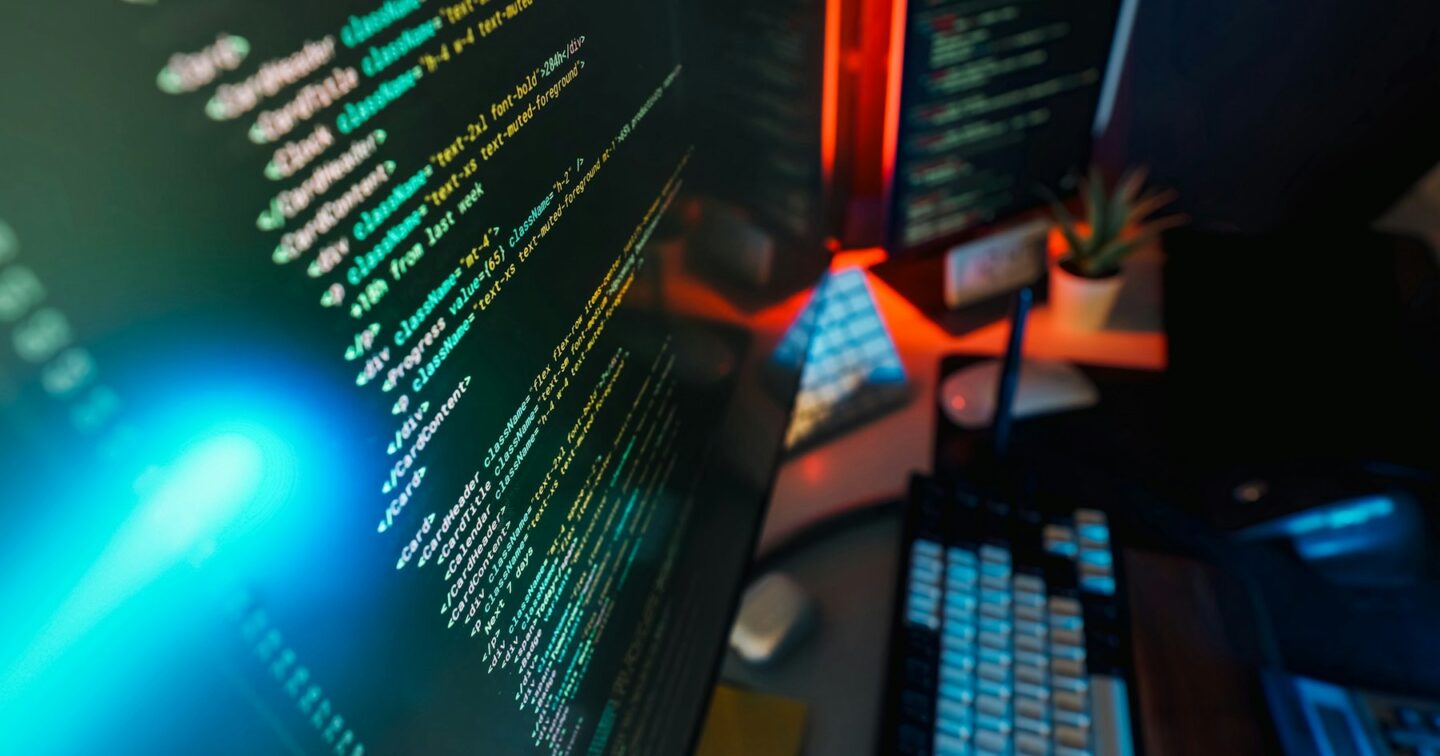 Monitor showing colour-highlighted front-end code beside a mechanical keyboard in a developer workspace